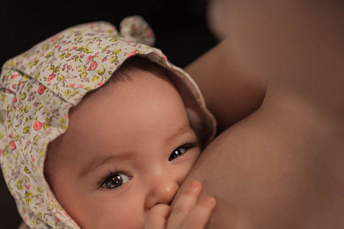 Close-up of a baby in a floral bonnet nursing, looking at the camera