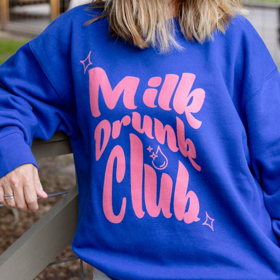 "Person wearing a blue sweatshirt with 'Milk Drunk Club' text, standing outdoors."