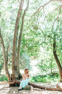 Woman sitting on a log under a tree in a forest - best lactation consultant near me