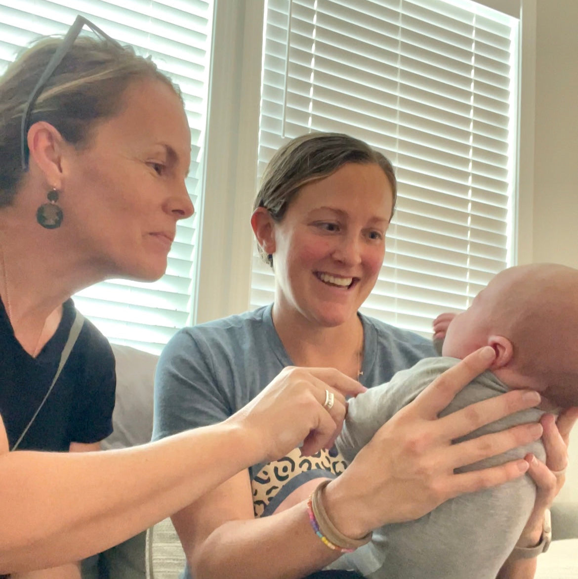 Two women holding a baby indoors with blinds in the background - consultant lactation